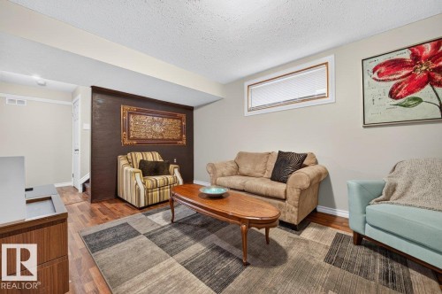 Spacious living area featuring wood-finish flooring, a neutral color palette, a rectangular window with blinds, and a built-in wall element with textured finish - 17411 90 Street Nw, Edmonton, AB - Indoor Photo Showing Living Room