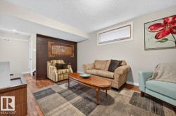 Spacious living area featuring wood-finish flooring, a neutral color palette, a rectangular window with blinds, and a built-in wall element with textured finish - 