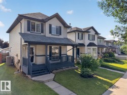 Two-story home with light-toned siding, dark shutters, and a covered front porch featuring dark railings - 