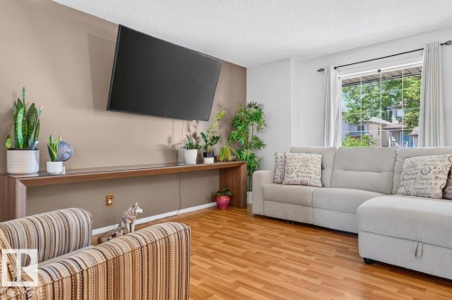 Living area with wood-finish flooring, a large window providing natural light, and a built-in wood-finish media console - 17411 90 Street Nw, Edmonton, AB - Indoor Photo Showing Living Room