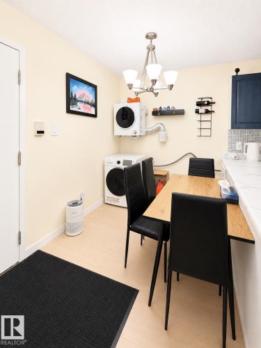 Compact laundry area featuring a stacked washer and wall-mounted dryer, complemented by light wood-finish flooring and a contemporary chandelier - #101 11825 71 St Nw, Edmonton, AB - Indoor