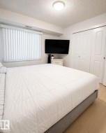 Bright bedroom featuring a large window with vertical blinds, light wood-finish flooring, a flush-mount ceiling light, and white bi-fold closet doors - 