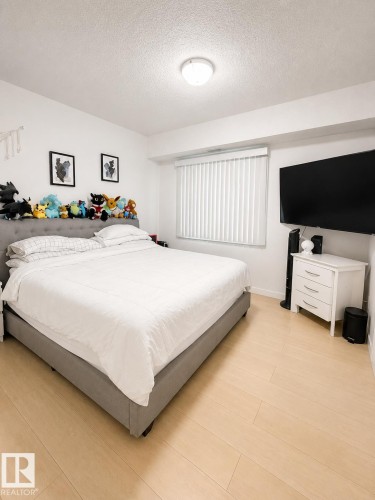 Bedroom featuring wood-finish flooring, a window with vertical blinds, and a flush-mount ceiling light - #101 11825 71 St Nw, Edmonton, AB - Indoor Photo Showing Bedroom