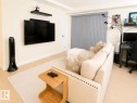 Bright living area featuring wood-finish flooring, light-toned walls, a white paneled door, vertical window blinds, and built-in floating shelves - #101 11825 71 St Nw, Edmonton, AB  - Indoor 