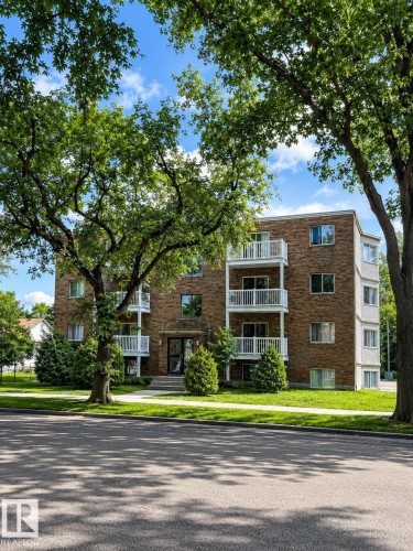 Multi-story building featuring brick and stucco exterior, multiple private balconies with white railings, and a prominent main entrance - #101 11825 71 St Nw, Edmonton, AB - Outdoor With Facade