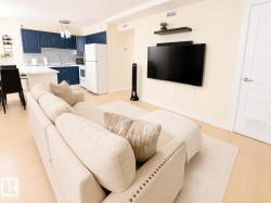 Open-concept living area featuring light wood-finish flooring, a wall-mounted television space, and a kitchen with navy cabinetry - 
