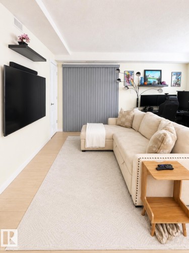 Living area featuring light wood-finish flooring with a neutral area rug, soft beige walls, and vertical blinds - #101 11825 71 St Nw, Edmonton, AB - Indoor