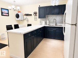 Modern kitchen featuring dark blue cabinetry, light marble-look countertops, and a white tile backsplash - 