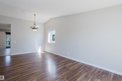 Spacious interior room featuring rich wood-finish flooring, a vaulted ceiling, and a decorative chandelier - 