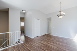 Open-concept living space with vaulted ceilings, wood-finish flooring, a decorative chandelier, and white baseboards - 