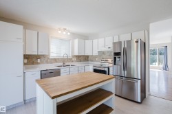 Kitchen featuring white cabinetry, stone backsplash, and stainless steel appliances - 