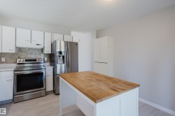 Kitchen featuring a wood-finish island, white cabinetry, stainless steel appliances, and a stone-tile backsplash - 