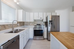 Modern kitchen featuring white cabinetry, light countertops, and a full suite of stainless steel appliances - 