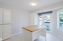 Kitchen area featuring a central island with a wood-finish countertop, white cabinetry, and light-toned tile flooring - 