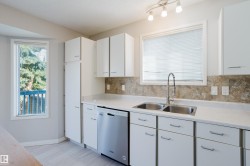 Well-appointed kitchen featuring white cabinetry, light-toned countertops, a dual basin stainless steel sink with a gooseneck faucet, a stainless steel dishwasher, and a tiled backsplash - 