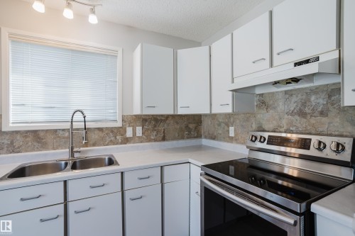 Kitchen featuring white cabinetry, light-toned countertops, a stainless steel electric range, and a dual basin sink with a gooseneck faucet - 337 Pearson Crescent Nw, Edmonton, AB - Indoor Photo Showing Kitchen With Double Sink