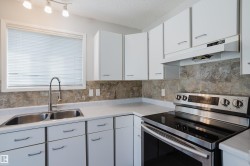 Kitchen featuring white cabinetry, light-toned countertops, a stainless steel electric range, and a dual basin sink with a gooseneck faucet - 