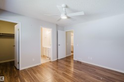 Spacious room featuring wood-finish flooring, light gray walls, and a white ceiling fan with integrated lighting - 