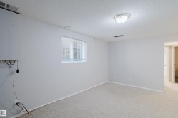 Spacious room featuring light-colored carpeting, white walls, and a ceiling-mounted light fixture - 