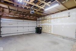 Spacious garage featuring a concrete floor, overhead fluorescent lighting, exposed wood ceiling joists, and a sectional garage door with an automatic opener - 