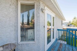 Textured exterior wall featuring a window with blinds, double glass-paneled doors, and an outdoor deck with blue railing - 