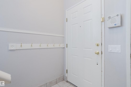 Entryway featuring a paneled door with brass hardware, tile flooring, a wall-mounted coat rack with brass hooks, and an alarm system keypad - 337 Pearson Crescent Nw, Edmonton, AB - Indoor Photo Showing Other Room