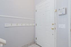 Entryway featuring a paneled door with brass hardware, tile flooring, a wall-mounted coat rack with brass hooks, and an alarm system keypad - 