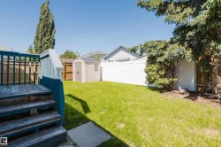 Spacious backyard featuring a green lawn, a blue-painted wood deck with stairs, and a light-colored storage shed - 