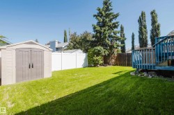 Spacious backyard featuring a manicured lawn, a blue-painted wooden deck with railings, and a tan storage shed - 