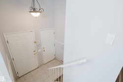 Entry foyer featuring two panel doors, ceramic tile flooring, a metal and glass semi-flush light fixture, and a white staircase railing - 