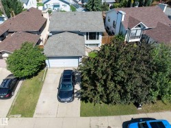 Property exterior featuring a light gray shingle roof, attached two-car garage, multiple mature trees, and a concrete driveway - 
