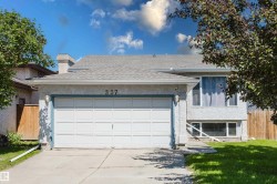 Stucco exterior featuring a dual-car garage with a panel door, an asphalt shingle roof, and a concrete driveway - 