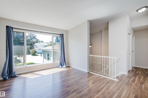 Spacious room with wood-finish flooring, a large multi-pane window, and a white metal staircase railing - 337 Pearson Crescent Nw, Edmonton, AB - Indoor