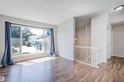 Spacious room with wood-finish flooring, a large multi-pane window, and a white metal staircase railing - 
