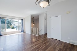 Spacious room featuring wood-finish flooring, a large multi-pane window, light gray walls, and a chandelier - 