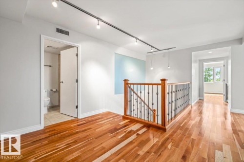 Hardwood flooring throughout a bright interior featuring a staircase with wood newel posts and wrought iron spindles - #202 10010 119 St Nw, Edmonton, AB - Indoor Photo Showing Other Room