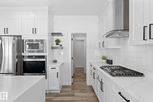 Contemporary kitchen featuring white shaker cabinetry, stainless steel appliances, a gas range with range hood, light-toned countertops, and wood-finish flooring - 59 Willow Link, Fort Saskatchewan, AB - Indoor Photo Showing Kitchen With Upgraded Kitchen
