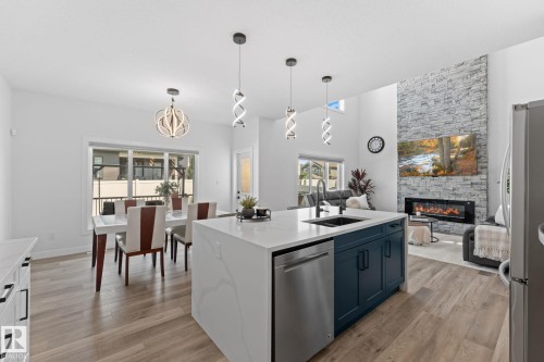 Open-concept main living area featuring a large kitchen island with quartz countertops, a modern fireplace with a stacked stone surround, wood-finish flooring, and contemporary pendant lighting - 59 Willow Link, Fort Saskatchewan, AB - Indoor Photo Showing Kitchen With Upgraded Kitchen