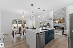 Open-concept main living area featuring a large kitchen island with quartz countertops, a modern fireplace with a stacked stone surround, wood-finish flooring, and contemporary pendant lighting - 