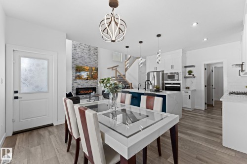 Open concept living area featuring wood-finish flooring, a contemporary fireplace with a stone-clad accent wall, a kitchen island with seating, pendant lighting, and stainless steel appliances - 59 Willow Link, Fort Saskatchewan, AB - Indoor