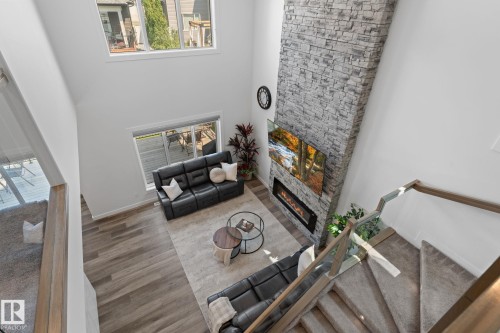 Two-story living area featuring a stacked stone fireplace with an integrated linear electric insert, a mounted television, wood-finish flooring, and a large window with a roller shade - 59 Willow Link, Fort Saskatchewan, AB - Indoor Photo Showing Other Room With Fireplace