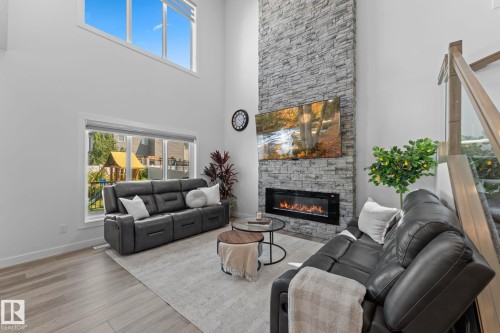 Living area featuring a floor-to-ceiling stacked stone fireplace, linear electric insert, and wood-finish flooring - 59 Willow Link, Fort Saskatchewan, AB - Indoor Photo Showing Living Room With Fireplace