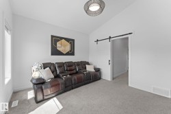 Carpeted interior space featuring a modern barn door, vaulted ceiling, and an architectural light fixture - 
