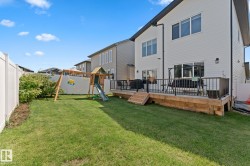 Expansive backyard featuring a large wooden deck with dark railings, a manicured lawn, and white privacy fencing - 