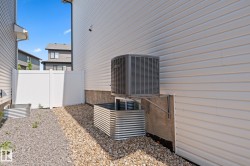 Side yard featuring white vinyl siding, a white privacy fence, an exterior HVAC unit, and two galvanized steel window wells - 
