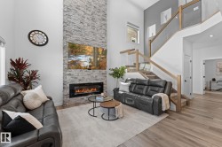 Two-story living area featuring a stacked stone fireplace with an electric insert, wood-finish flooring, and a glass-paneled staircase with natural wood handrails - 
