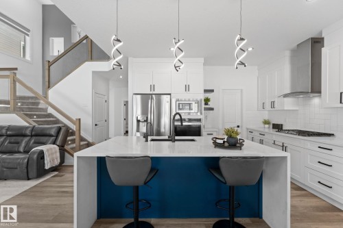 Contemporary kitchen featuring a large island with a waterfall countertop and contrasting blue paneling, white shaker-style cabinetry, stainless steel appliances, and wood-finish flooring - 59 Willow Link, Fort Saskatchewan, AB - Indoor Photo Showing Kitchen With Upgraded Kitchen