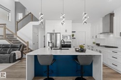 Contemporary kitchen featuring a large island with a waterfall countertop and contrasting blue paneling, white shaker-style cabinetry, stainless steel appliances, and wood-finish flooring - 