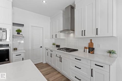 Modern kitchen featuring white shaker-style cabinetry, a stainless steel range hood, built-in microwave and oven, a gas cooktop, and light-toned countertops - 59 Willow Link, Fort Saskatchewan, AB - Indoor Photo Showing Kitchen