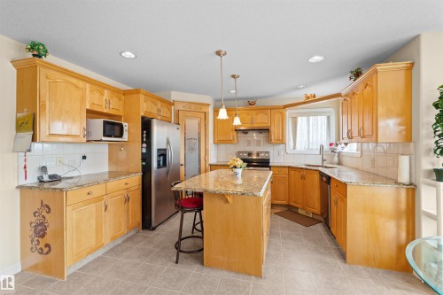 Kitchen featuring wood cabinetry, light granite-style countertops, and a central island with pendant lighting - 7622 168A Avenue, Edmonton, AB - Indoor Photo Showing Kitchen